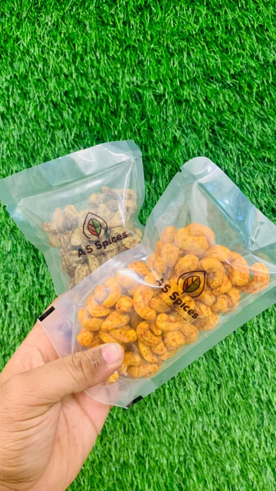 Two pouches of spiced cashews held in a hand