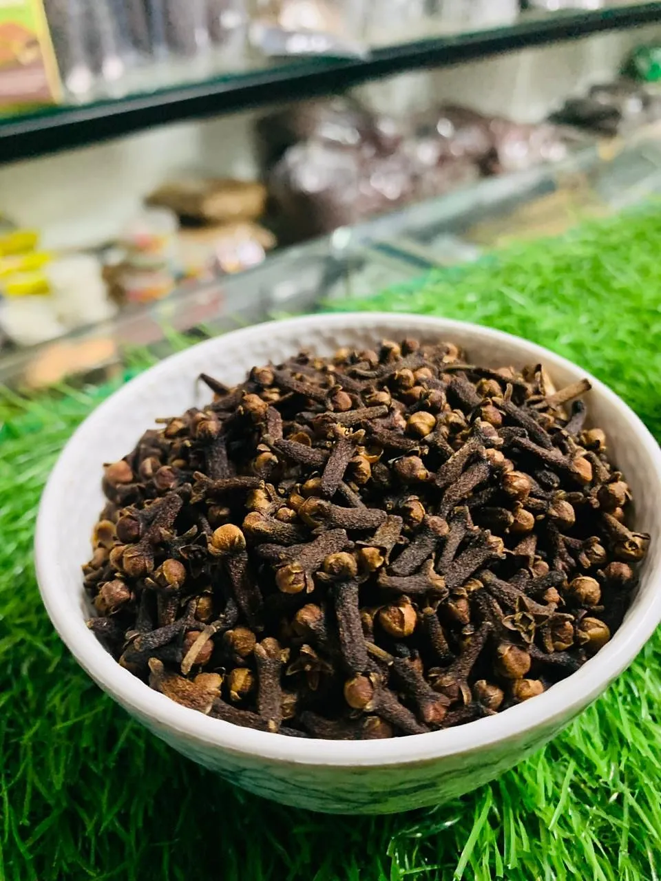Whole dried cloves heaped in a white bowl on green grass